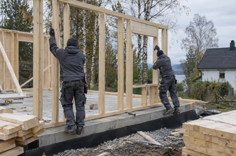 To tømrere reiser en trevegg på et nybygg